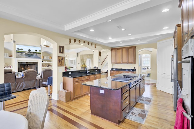 kitchen with a kitchen island, light wood-type flooring, stainless steel gas stovetop, arched walkways, and a sink