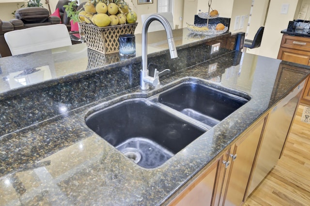 room details with a sink, dark stone counters, brown cabinets, and light wood finished floors