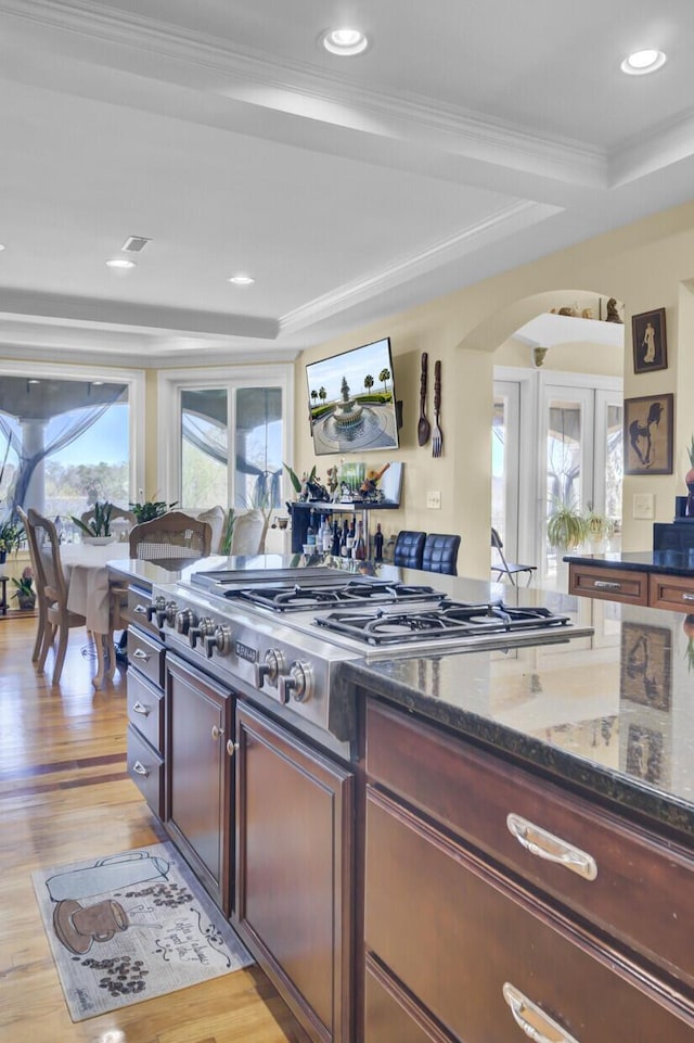 kitchen with stainless steel gas cooktop, dark stone counters, arched walkways, crown molding, and light wood-type flooring