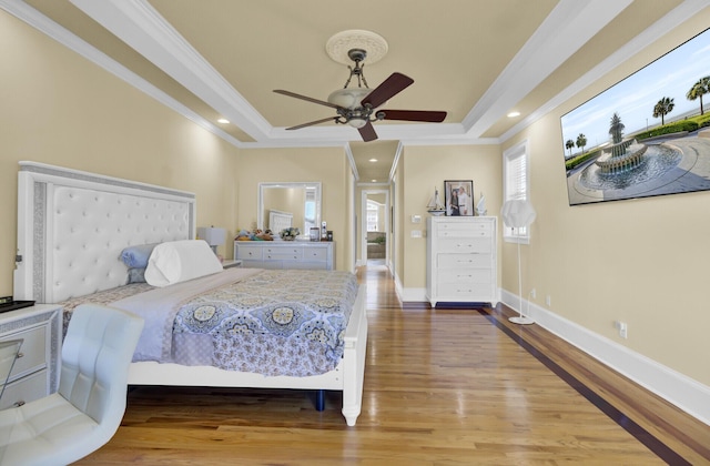 bedroom featuring a tray ceiling, wood finished floors, baseboards, and ornamental molding
