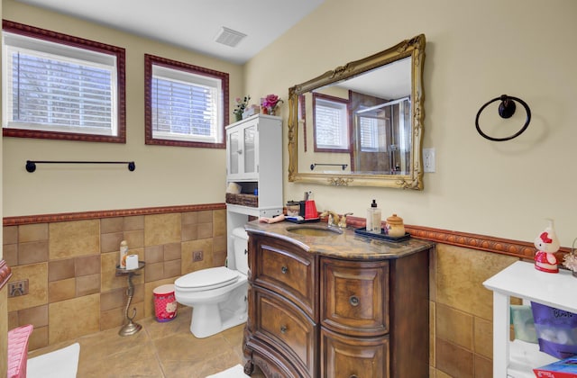 full bath with visible vents, toilet, wainscoting, a stall shower, and tile walls