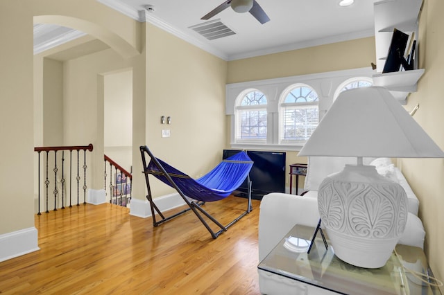 living area featuring wood finished floors, visible vents, arched walkways, and ornamental molding