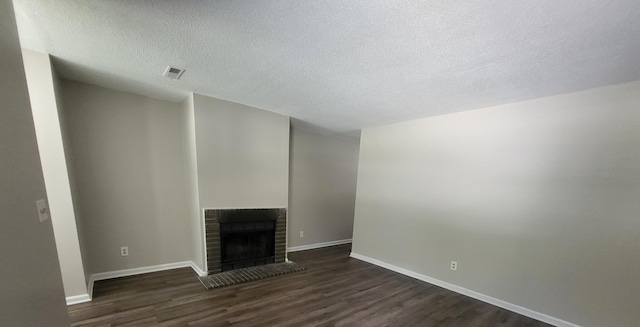 unfurnished living room with a textured ceiling, dark hardwood / wood-style flooring, and a brick fireplace