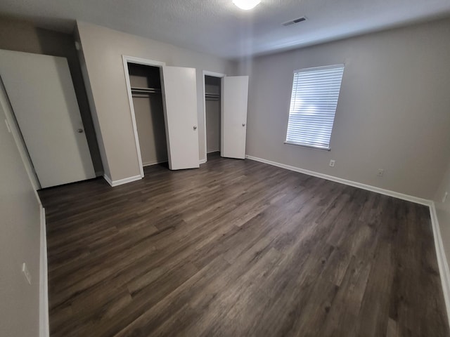 unfurnished bedroom featuring two closets, dark hardwood / wood-style flooring, and a textured ceiling