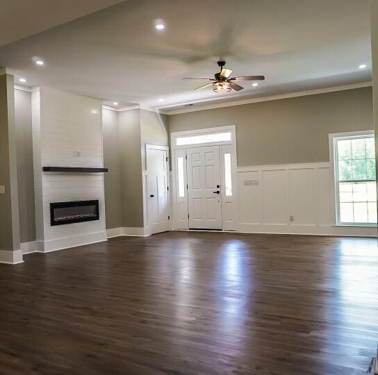 unfurnished living room with a fireplace, dark wood-type flooring, ceiling fan, and ornamental molding