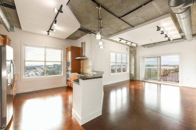 kitchen with dark stone counters, wall chimney exhaust hood, stainless steel appliances, and decorative light fixtures