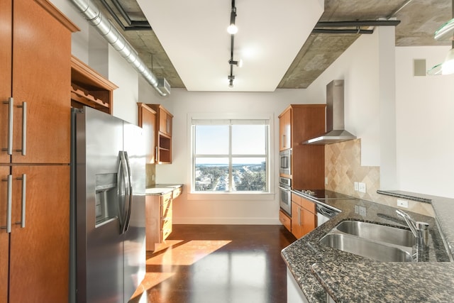 kitchen with track lighting, wall chimney range hood, sink, dark stone countertops, and stainless steel appliances