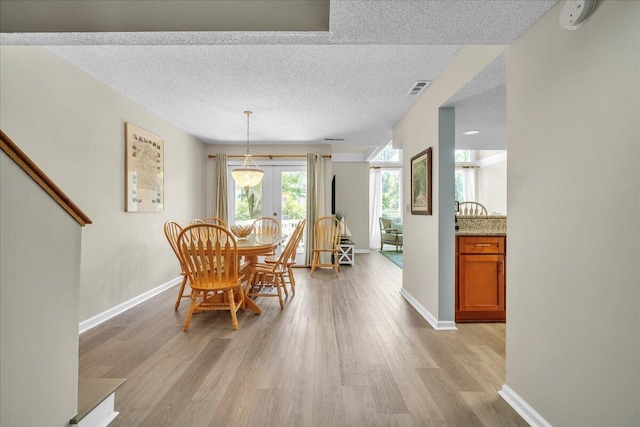 dining area with light wood-type flooring, a textured ceiling, and french doors