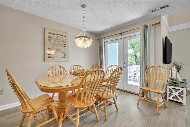 dining space featuring a textured ceiling, an inviting chandelier, french doors, and light wood-type flooring