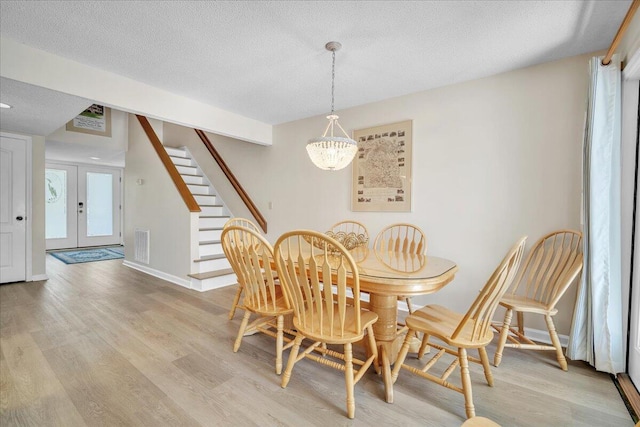 dining room with a chandelier, a textured ceiling, french doors, and light wood-type flooring