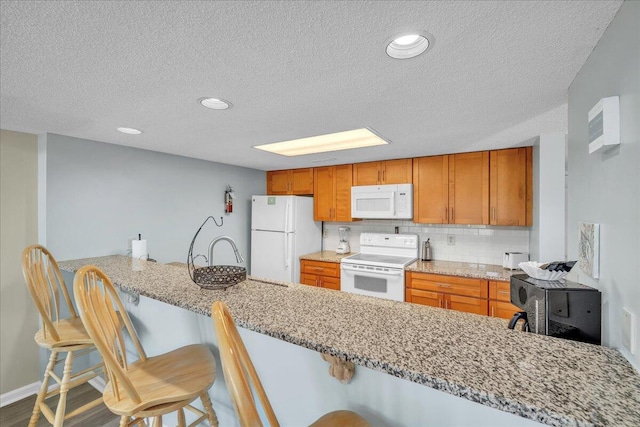 kitchen with a kitchen breakfast bar, white appliances, kitchen peninsula, and tasteful backsplash