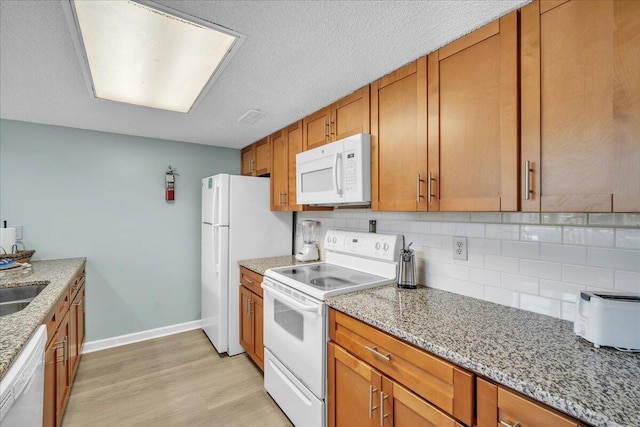 kitchen featuring light stone countertops, white appliances, sink, backsplash, and light hardwood / wood-style flooring