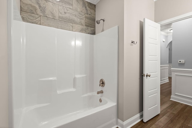 bathroom with a wainscoted wall, a decorative wall, bathing tub / shower combination, and wood finished floors