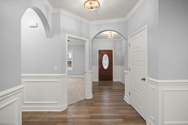 foyer entrance featuring ornamental molding, arched walkways, dark wood-style flooring, and wainscoting