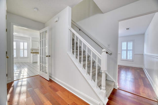 stairway with wood-type flooring, a textured ceiling, visible vents, and a wealth of natural light