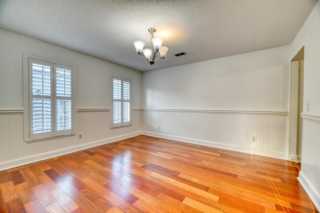 unfurnished room featuring a chandelier, a textured ceiling, visible vents, wainscoting, and hardwood / wood-style floors