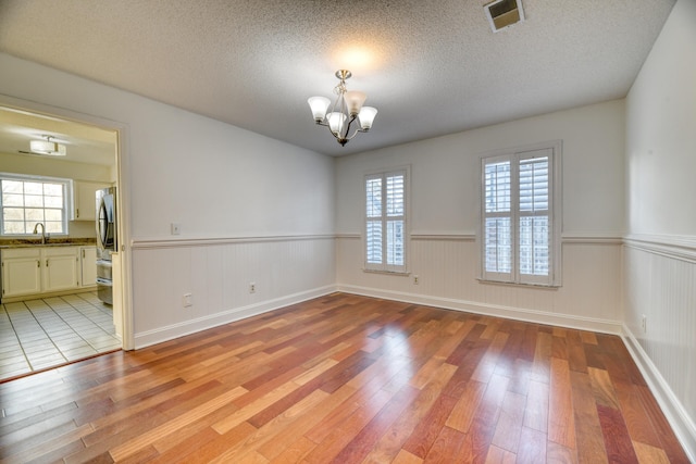 empty room with visible vents, a wainscoted wall, an inviting chandelier, light wood-type flooring, and a sink