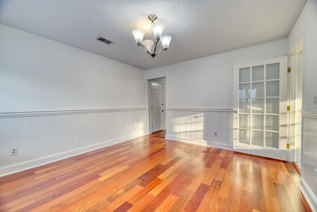 unfurnished room with a textured ceiling, visible vents, a chandelier, and hardwood / wood-style floors