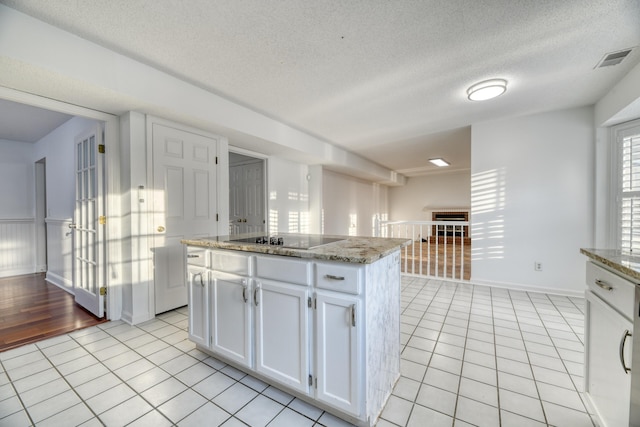 kitchen with white cabinets, visible vents, black electric stovetop, and light tile patterned floors