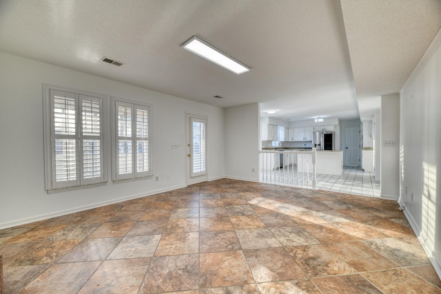 unfurnished living room with a textured ceiling, stone finish floor, visible vents, and baseboards