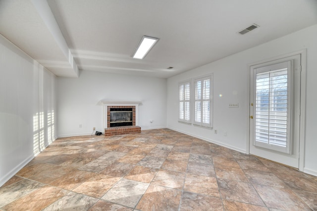 unfurnished living room featuring a brick fireplace, visible vents, stone finish flooring, and baseboards