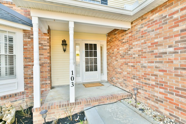 doorway to property with a porch and brick siding