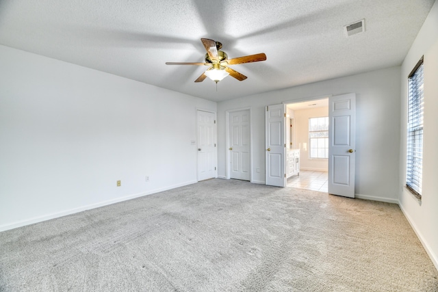 unfurnished bedroom featuring baseboards, visible vents, ensuite bath, carpet, and a textured ceiling