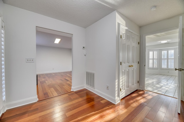 hall featuring baseboards, a textured ceiling, visible vents, and wood finished floors