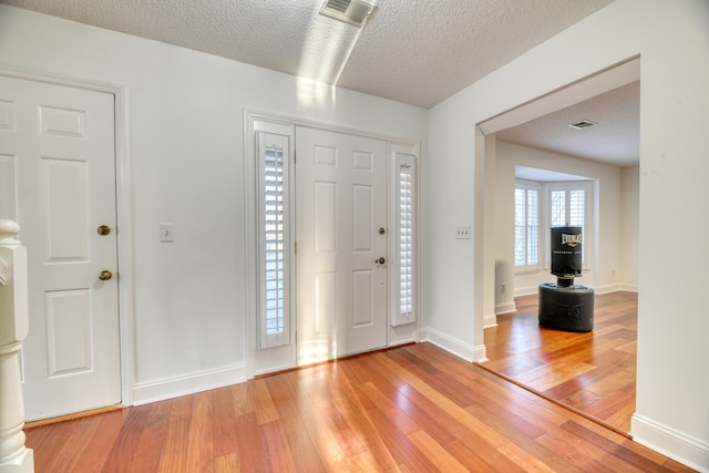 entrance foyer with light wood finished floors, baseboards, visible vents, and a textured ceiling