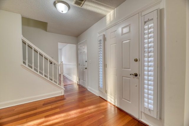 foyer featuring wood-type flooring, visible vents, stairway, a textured ceiling, and baseboards