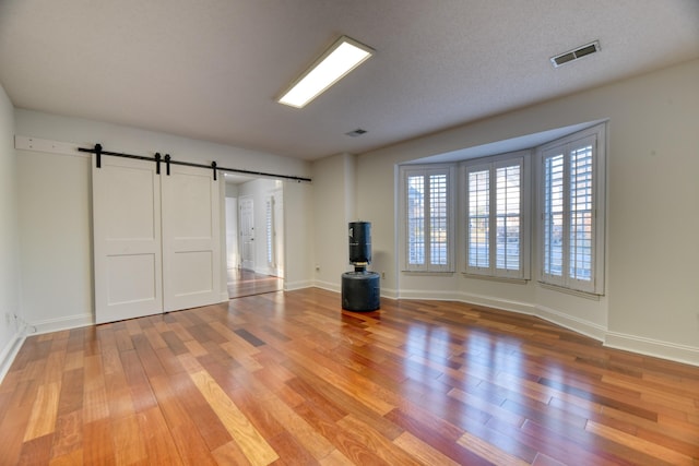 unfurnished living room featuring a barn door, visible vents, light wood-style flooring, and baseboards