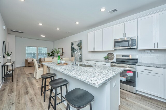 kitchen featuring stainless steel appliances, a sink, visible vents, tasteful backsplash, and a center island with sink