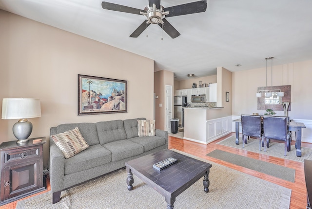 living room with ceiling fan with notable chandelier and light hardwood / wood-style floors