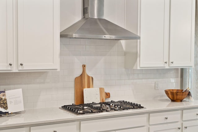 kitchen with stainless steel gas cooktop, decorative backsplash, white cabinetry, and wall chimney range hood