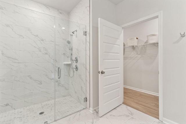 full bathroom featuring a spacious closet, a shower stall, marble finish floor, and baseboards