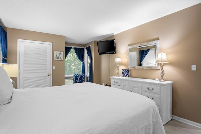 bedroom featuring lofted ceiling, light wood-style flooring, and baseboards