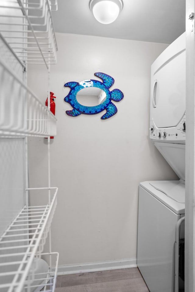 washroom featuring laundry area, stacked washer / dryer, wood finished floors, and baseboards