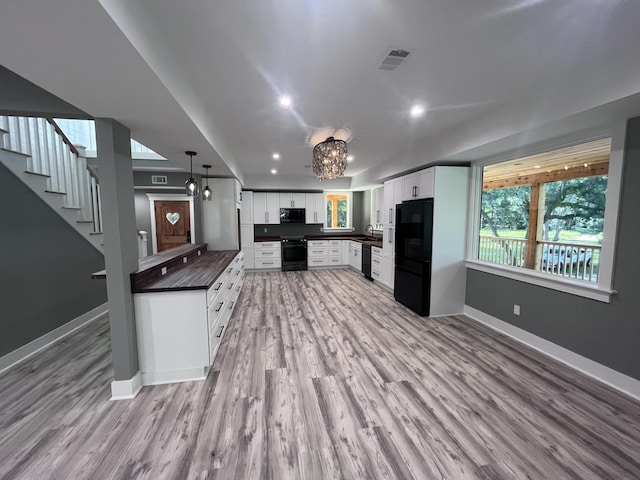 kitchen with sink, decorative light fixtures, light wood-type flooring, white cabinets, and black appliances