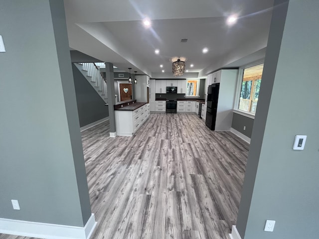 kitchen featuring white cabinetry, decorative light fixtures, light hardwood / wood-style flooring, and black appliances