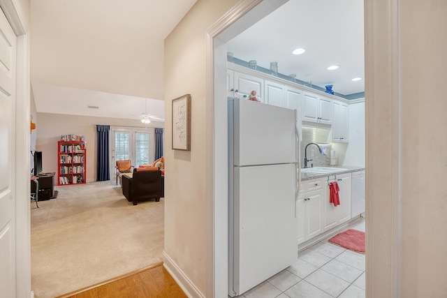 kitchen with white appliances, sink, light colored carpet, and white cabinetry