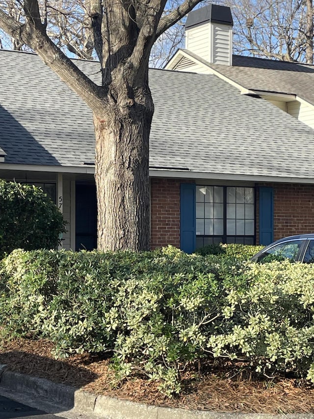 view of side of home featuring brick siding, a chimney, and roof with shingles