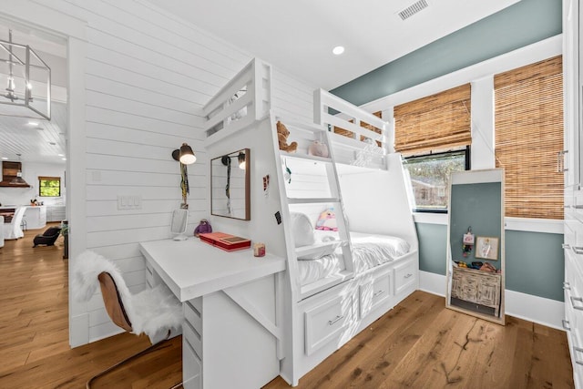 bedroom with wood walls, hardwood / wood-style flooring, and an inviting chandelier