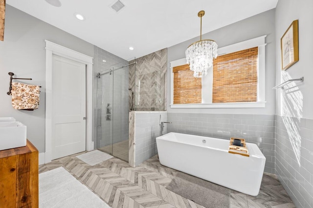 bathroom with independent shower and bath, tile walls, and an inviting chandelier