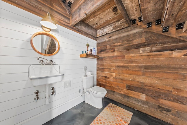 bathroom with concrete flooring, wood walls, sink, toilet, and wooden ceiling