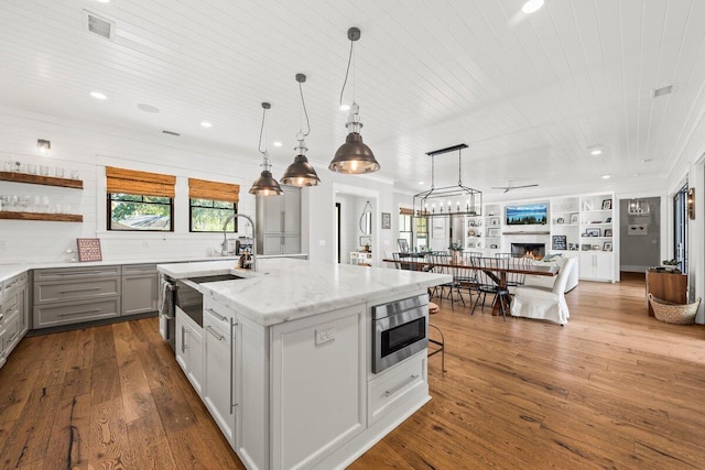 kitchen featuring a center island with sink, light stone counters, hardwood / wood-style floors, hanging light fixtures, and sink