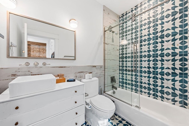 full bathroom featuring toilet, vanity, bath / shower combo with glass door, and tile walls