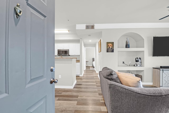 hallway with built in shelves, crown molding, and light hardwood / wood-style floors