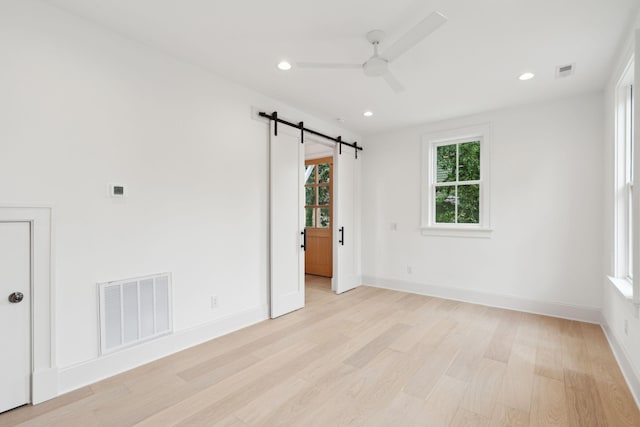 spare room with a barn door, light wood-type flooring, and ceiling fan