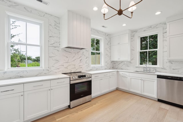 kitchen with appliances with stainless steel finishes, light wood-type flooring, an inviting chandelier, and white cabinets