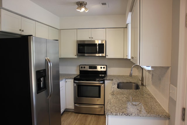 kitchen featuring stainless steel appliances, white cabinetry, light stone countertops, and sink